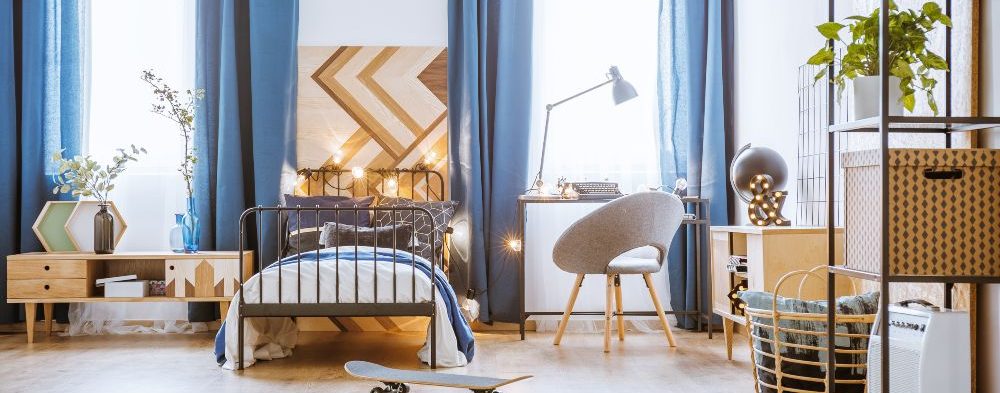 Skateboard next to the bed in bedroom interior with blue drapes and patterned panel
